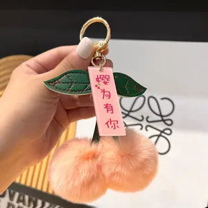 Detailed close-up of pink cherry plush keychain with green faux leather leaves and gold clasp