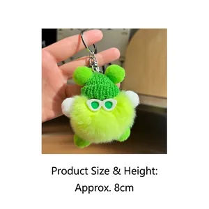 Detail showing an 8cm green fuzzy monster plush charm with hat and glasses in hand