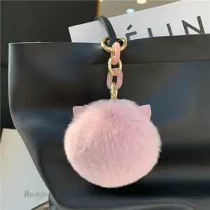 Detailed close-up of fluffy pink faux fur keychain with cat ears on a black leather tote bag