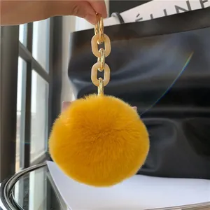 Close-up of bright yellow faux fur pompom keychain with chic gold and resin chain