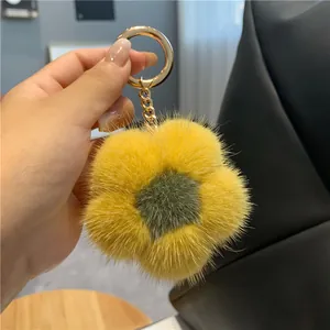 Détail d'un porte-clés fleur en fourrure jaune avec anneau doré sur un sac en cuir