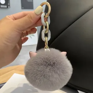 Detail of grey plush cat ear keychain with gold chain on a black leather handbag