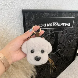 Close-up of a fluffy white puppy plush keychain with a gold ring and brown ribbon