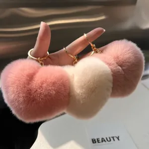 Drie pluche hartvormige sleutelhangers in roze, crème en paars met gouden ringdetails