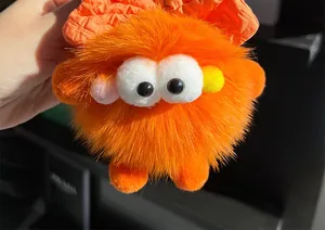 Detail van de pluizige oranje pluche monster sleutelhanger met grote ogen en een strikje