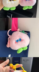 Close-up of a fluffy pink plush keychain with blue eyes attached to a blue canvas bag