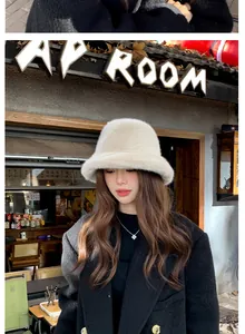 Détail d'un chapeau bob en fausse fourrure crème porté avec un manteau noir chic