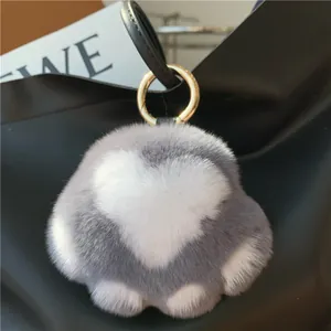 Close-up of grey and white cat paw plush keychain with golden ring on a black bag