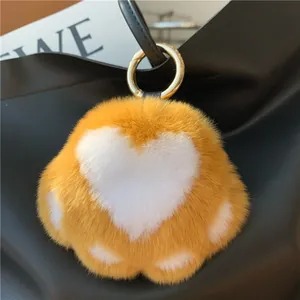Close-up of fluffy orange cat paw plush keychain with golden metal clasp on black leather bag