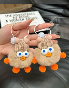 Detailed close-up of cute plush duck keychain with soft fur and knitted hat held in hand