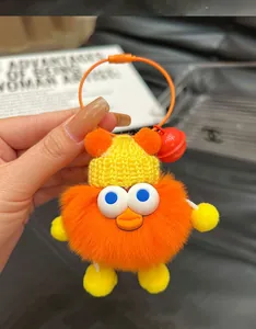 Detail of cute orange plush monster keychain with yellow knit hat and a red bell