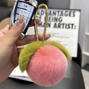 Close-up of a soft pink rabbit fur peach keychain with green leaves and a gold clasp