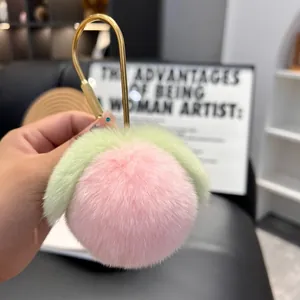 Close-up of a soft pink plush peach keychain with green leaves and a gold metal hook