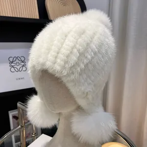 Detailed knit texture of white mink fur hat with plush fox fur pompoms and ear flaps