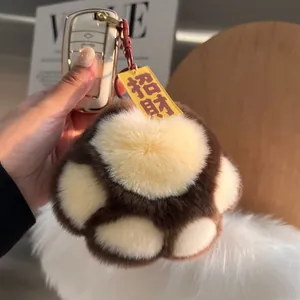 Detail of soft brown plush paw charm with red metal ring and yellow fortune tag