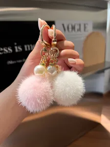 Close-up of pink and white faux fur pompom keychain with pearl detail and gold chain