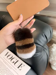 Close-up of fluffy striped faux rabbit fur tail keychain on a black leather background