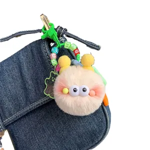 Cute plush monster keychain with fuzzy balls and colorful letter beads on denim background
