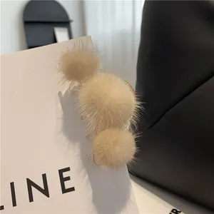 Nahaufnahme der beigefarbenen Nerzpelz-Pompons auf einer goldenen Metall-Haarklammer