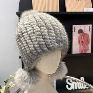 Detail of grey mink fur knit hat with three fluffy fox fur pom-poms on earflaps
