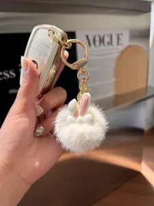 Close-up of a white fluffy rabbit fur ball keychain with pink ears and gold chain