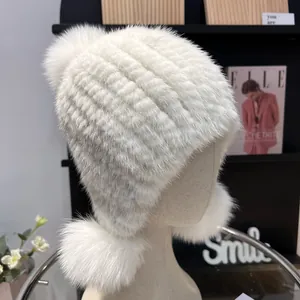 Detail of white mink fur hat featuring three fluffy fox fur pom-poms and ear protection