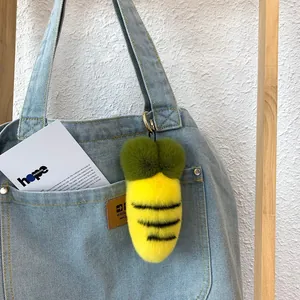 Plush bee-themed carrot keychain charm with metal hook on light blue denim bag