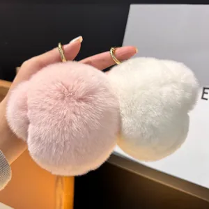 Détail de pompons en peluche roses et blancs avec anneaux dorés tenus à la main