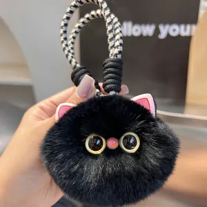 Close-up of cute black plush cat keychain with pink ears and large yellow eyes on woven cord