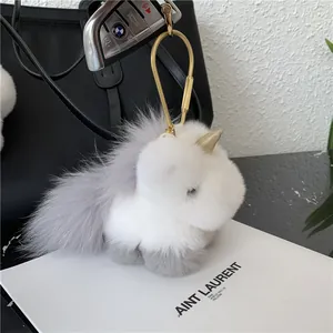 Detail of plush unicorn bag charm with fluffy grey fur and golden horn on leather bag