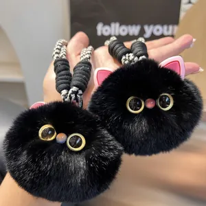 Detail of two black plush cat keychains with fluffy fur and large yellow eyes