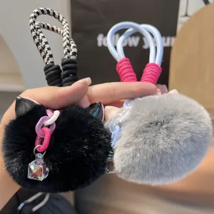Detail of plush cat ear pom keychain with braided rope and iridescent cube charm