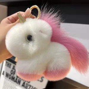 Close-up of fluffy pink and white plush unicorn keychain with a shiny gold horn