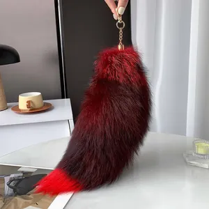 Close-up of fluffy faux fur fox tail keychain in burgundy and red with gold metal clasp