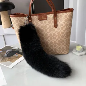 Detail view of a large fluffy black fox fur keychain hanging on a brown luxury tote bag