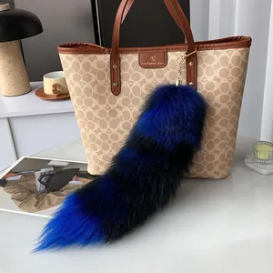 Detail of blue and black striped faux fur fox tail charm with gold metal clasp on a bag