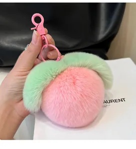 Close-up of a plush pink peach keychain with green leaves held against a stylish black bag