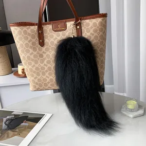 Close-up of black fluffy fur tail keychain with gold clasp on a brown handbag