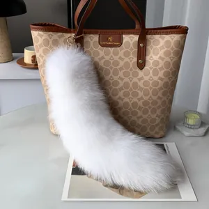 Close-up of fluffy white faux fur fox tail charm with gold clasp on a brown handbag