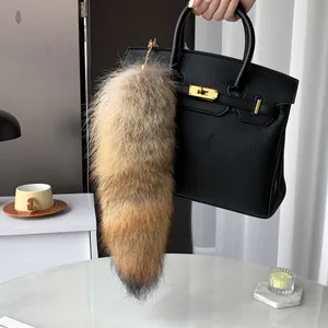 Lush faux fur fox tail bag charm with golden metal clasp on a textured leather handbag