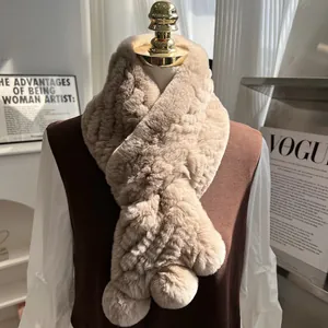 Detail of warm beige rabbit fur scarf featuring a cross-over design and plush pom-poms