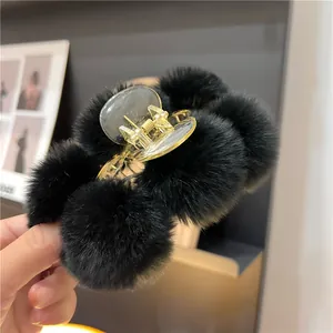 Close-up of fluffy black faux fur pom-poms on a gold hair claw clip for winter styling
