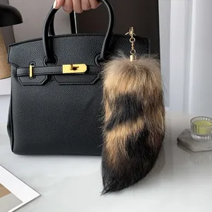 Detail of real fox fur tail charm with gold chain on black leather handbag