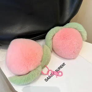 Plush peach-shaped keychain with soft pink fur and green leaves on a black bag