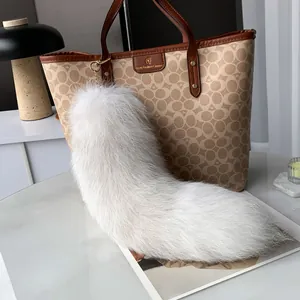 Macro view of plush white faux fur fox tail pendant with metallic ring on a bag