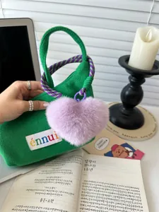 Close-up of green felt mini tote bag featuring a purple plush heart charm and woven handle