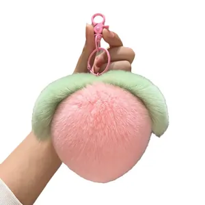 Plush peach-shaped keychain with pink faux fur and green leaf on white background