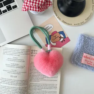 Close-up of fluffy pink heart-shaped faux fur keychain with woven lanyard on desk