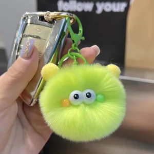Cute bright green plush pom-pom keychain with large eyes and ears on a car key