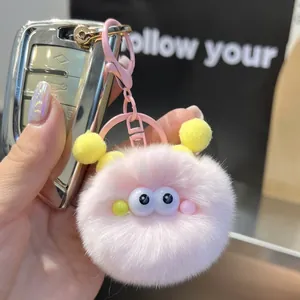 Detailed close-up of pink fluffy monster plush keychain with yellow pom-pom antennae and hook